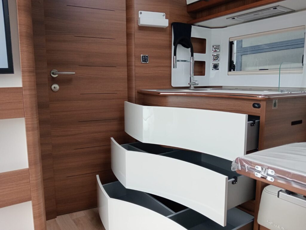 Cocina de la autocaravana Rapido I96M 2025 con frentes curvos en blanco brillante, extractor LED y grifo extraíble cromado