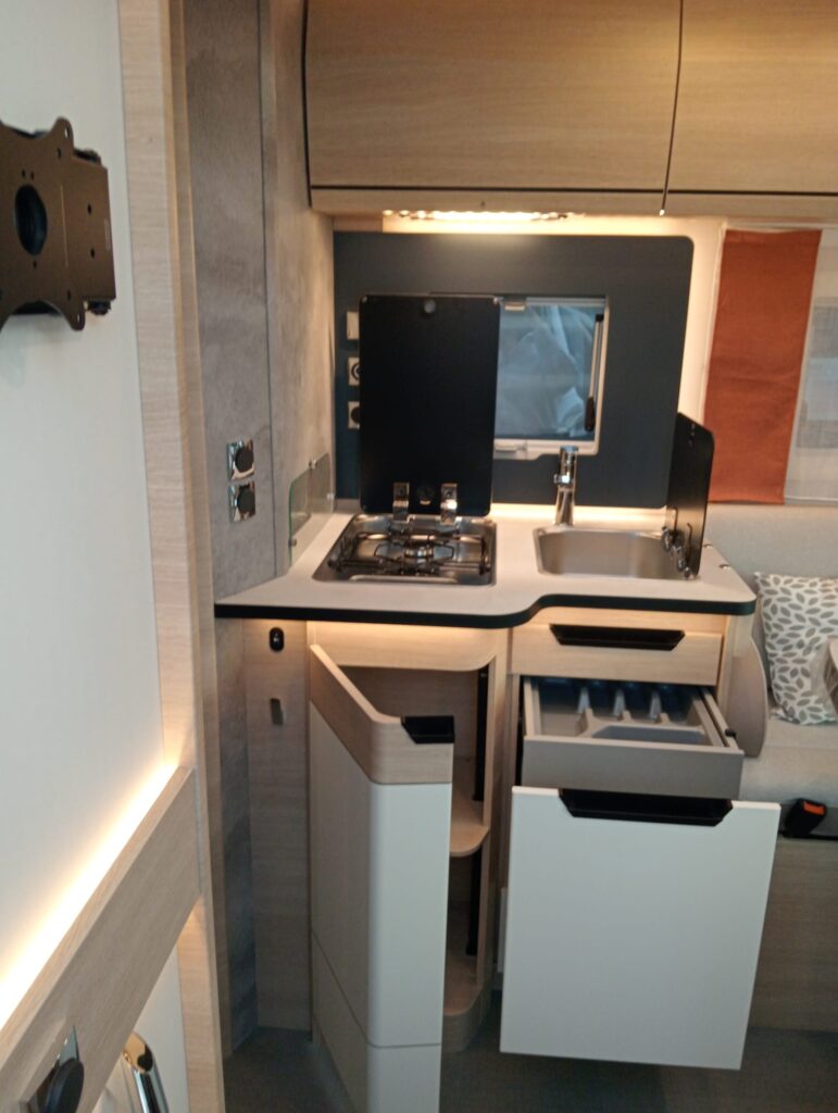 Cocina del Rapido C86 i con 2 fuegos, fregadero, protección en la ventana contra salpicaduras y amplios cajones y armario con cierre de seguridad.”